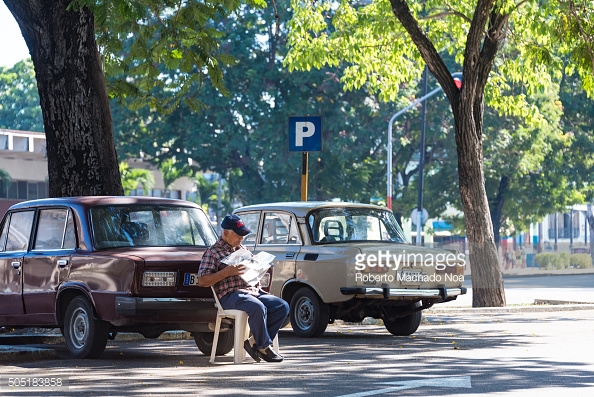 HAVANA CITY, HAVANA, CUBA - 2015/09/19: Cuba scenes: Senior man in-charge of car parking area sitting on a chair reading newspaper. (Photo by Roberto Machado Noa/LightRocket via Getty Images)